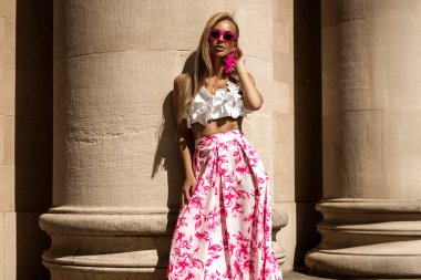 Pembe çiçekli yaz eteği ve şık fırfırlı bluzla şık, şık bir model güneşli bir yaz gününde şehrimizde şehvetli bir şekilde dolaşıyor. Açık havada fotoşop.