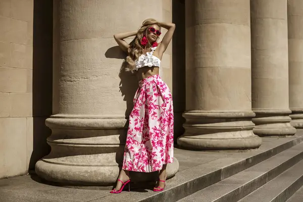 Pembe çiçekli yaz eteği ve şık fırfırlı bluzla şık, şık bir model güneşli bir yaz gününde şehrimizde şehvetli bir şekilde dolaşıyor. Açık havada fotoşop.