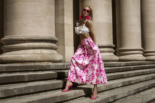 Pembe çiçekli yaz eteği ve şık fırfırlı bluzla şık, şık bir model güneşli bir yaz gününde şehrimizde şehvetli bir şekilde dolaşıyor. Açık havada fotoşop.