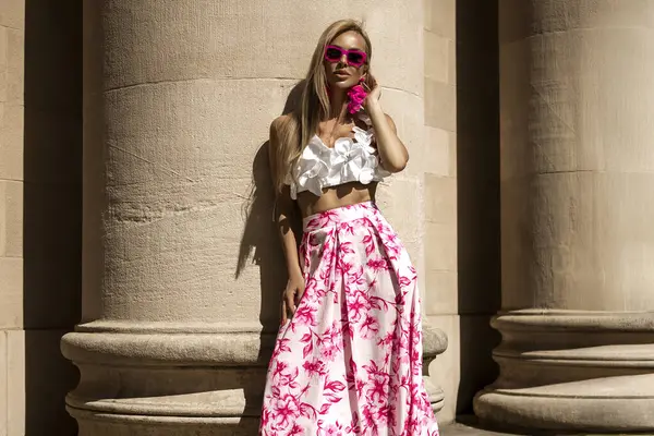 Pembe çiçekli yaz eteği ve şık fırfırlı bluzla şık, şık bir model güneşli bir yaz gününde şehrimizde şehvetli bir şekilde dolaşıyor. Açık havada fotoşop.