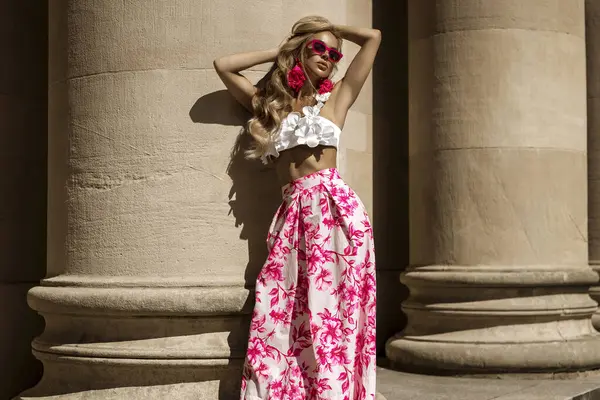 Pembe çiçekli yaz eteği ve şık fırfırlı bluzla şık, şık bir model güneşli bir yaz gününde şehrimizde şehvetli bir şekilde dolaşıyor. Açık havada fotoşop.