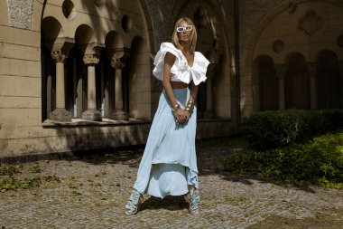 Uzun sarı saçlı, mavi etekli ve dalgalı bluzlu zarif manken güneşli bir yaz gününde şehrimizde şehvetli pozlar veriyor. Yaz modası.