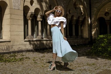 Uzun sarı saçlı, mavi etekli ve dalgalı bluzlu zarif manken güneşli bir yaz gününde şehrimizde şehvetli pozlar veriyor. Yaz modası.