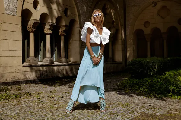 Uzun sarı saçlı, mavi etekli ve dalgalı bluzlu zarif manken güneşli bir yaz gününde şehrimizde şehvetli pozlar veriyor. Yaz modası.