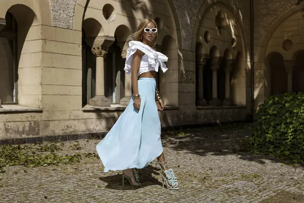 Uzun sarı saçlı, mavi etekli ve dalgalı bluzlu zarif manken güneşli bir yaz gününde şehrimizde şehvetli pozlar veriyor. Yaz modası.