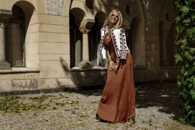 Şık bir yaz tulumu ve boho ceketiyle şık bir kadın model güneşli bir yaz gününde şehirde şehvetli pozlar veriyor. Yaz modası.