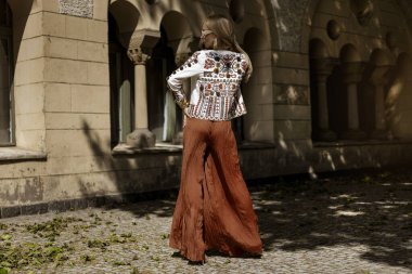 Şık bir yaz tulumu ve boho ceketiyle şık bir kadın model güneşli bir yaz gününde şehirde şehvetli pozlar veriyor. Yaz modası.