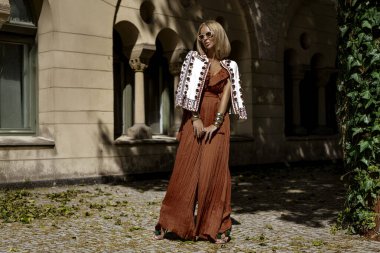 Şık bir yaz tulumu ve boho ceketiyle şık bir kadın model güneşli bir yaz gününde şehirde şehvetli pozlar veriyor. Yaz modası.