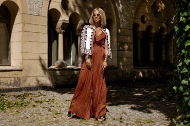 Şık bir yaz tulumu ve boho ceketiyle şık bir kadın model güneşli bir yaz gününde şehirde şehvetli pozlar veriyor. Yaz modası.