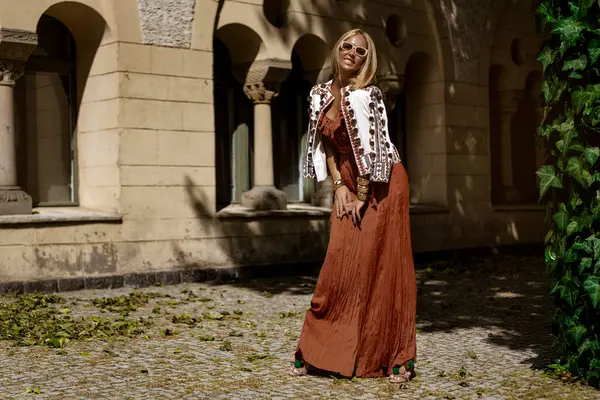 Şık bir yaz tulumu ve boho ceketiyle şık bir kadın model güneşli bir yaz gününde şehirde şehvetli pozlar veriyor. Yaz modası.