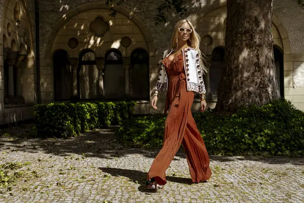 Şık bir yaz tulumu ve boho ceketiyle şık bir kadın model güneşli bir yaz gününde şehirde şehvetli pozlar veriyor. Yaz modası.