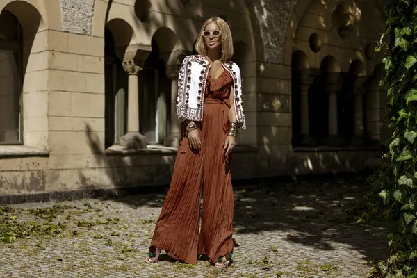 Şık bir yaz tulumu ve boho ceketiyle şık bir kadın model güneşli bir yaz gününde şehirde şehvetli pozlar veriyor. Yaz modası.