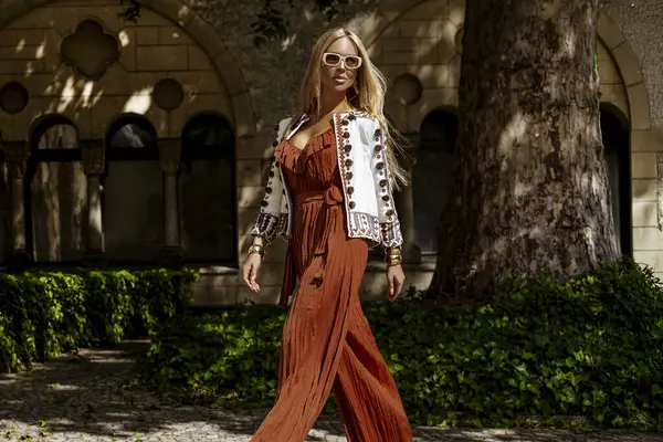 Şık bir yaz tulumu ve boho ceketiyle şık bir kadın model güneşli bir yaz gününde şehirde şehvetli pozlar veriyor. Yaz modası.