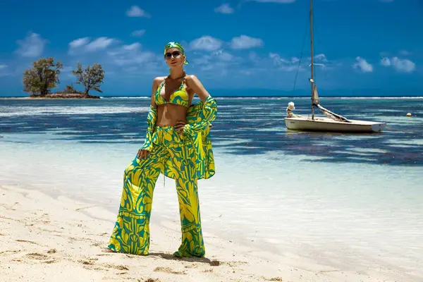 Seksi bikinili, eşarp ve plaj pantolonu giyen şık bir kadın Seyşeller 'deki kumlu sahilde poz veriyor. Plaj kıyafeti modası.