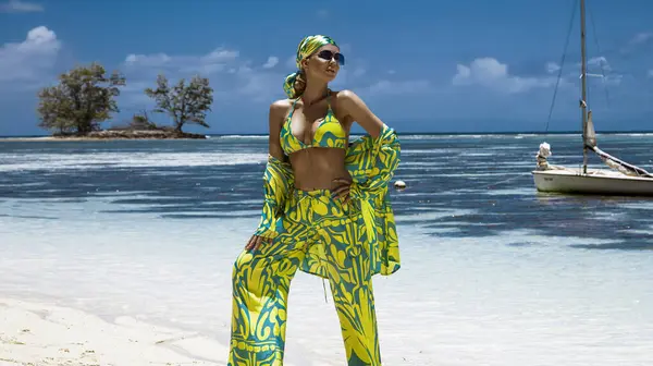 Seksi bikinili, eşarp ve plaj pantolonu giyen şık bir kadın Seyşeller 'deki kumlu sahilde poz veriyor. Plaj kıyafeti modası.
