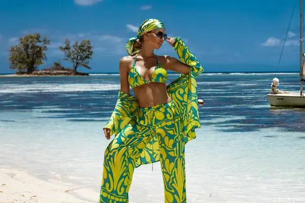 Seksi bikinili, eşarp ve plaj pantolonu giyen şık bir kadın Seyşeller 'deki kumlu sahilde poz veriyor. Plaj kıyafeti modası.