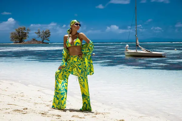 Seksi bikinili, eşarp ve plaj pantolonu giyen şık bir kadın Seyşeller 'deki kumlu sahilde poz veriyor. Plaj kıyafeti modası.