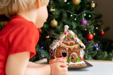 Bebek, arka planda bulanık Noel ağacı olan krema, şeker ve reçelli ev yapımı zencefilli çöreğe bakıyor. Aile Noeli.