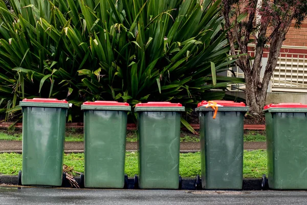 Australian garbage wheelie bins with red lids for household waste lined up on the street for council rubbish collection.