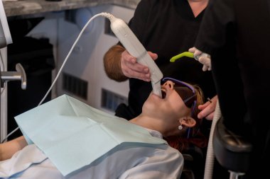 Genç kız dişlerinin ve diş etlerinin şeklini dijital olarak kaydetmek için dijital tarayıcı kullanan ortodontist, özel yapım plastik dizginleyiciler kullanıyor..