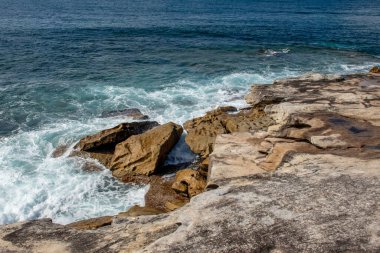 Okyanus dalgaları güneşli bir günde kıyı boyunca dokulu kum taşı oluşumlarına çarpar. Kraliyet Ulusal Parkı, NSW, Avustralya
