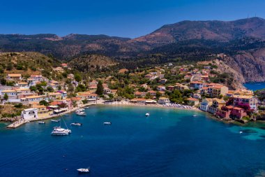 Assos 'un havadan görünüşü, Kefalonia. Turkuaz sularla çevrili bir yarımadada yuva yapmış güzel bir köy. Renkli evler, küçük plajlar ve körfezdeki tekneler. Arkaplanda yemyeşil tepeler ve dağlar var..