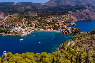 Assos 'un havadan görünüşü, Kefalonia. Turkuaz sularla çevrili bir yarımadada yuva yapmış güzel bir köy. Renkli evler, küçük plajlar ve körfezdeki tekneler. Arkaplanda yemyeşil tepeler ve dağlar var..