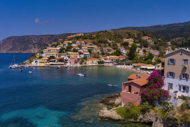 Assos 'un havadan görünüşü, Kefalonia. Turkuaz sularla çevrili bir yarımadada yuva yapmış güzel bir köy. Renkli evler, küçük plajlar ve körfezdeki tekneler. Arkaplanda yemyeşil tepeler ve dağlar var..