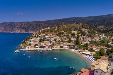 Assos 'un havadan görünüşü, Kefalonia. Turkuaz sularla çevrili bir yarımadada yuva yapmış güzel bir köy. Renkli evler, küçük plajlar ve körfezdeki tekneler. Arkaplanda yemyeşil tepeler ve dağlar var..