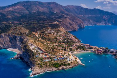 Assos 'un havadan görünüşü, Kefalonia. Turkuaz sularla çevrili bir yarımadada yuva yapmış güzel bir köy. Renkli evler, küçük plajlar ve körfezdeki tekneler. Arkaplanda yemyeşil tepeler ve dağlar var..