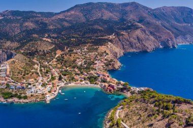 Assos 'un havadan görünüşü, Kefalonia. Turkuaz sularla çevrili bir yarımadada yuva yapmış güzel bir köy. Renkli evler, küçük plajlar ve körfezdeki tekneler. Arkaplanda yemyeşil tepeler ve dağlar var..