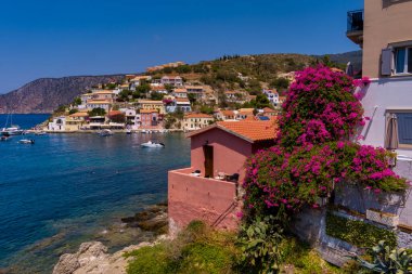 Assos 'un havadan görünüşü, Kefalonia. Turkuaz sularla çevrili bir yarımadada yuva yapmış güzel bir köy. Renkli evler, küçük plajlar ve körfezdeki tekneler. Arkaplanda yemyeşil tepeler ve dağlar var..
