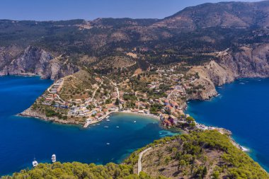 Assos 'un havadan görünüşü, Kefalonia. Turkuaz sularla çevrili bir yarımadada yuva yapmış güzel bir köy. Renkli evler, küçük plajlar ve körfezdeki tekneler. Arkaplanda yemyeşil tepeler ve dağlar var..