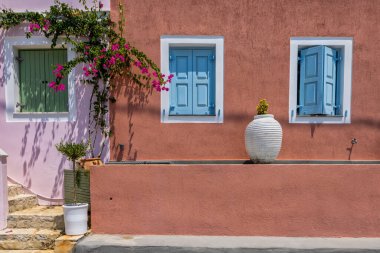 Assos, Kefalonia 'da güzel, pembe duvarlı bir ev. Parlak mavi panjurlar ve beyaz süslemeler, canlı görünüme karşı çarpıcı bir kontrast oluşturuyor. Pembe begonviller.