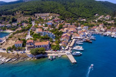Fiskardo 'nun havadan görünüşü, Kefalonia. Turkuaz sularla çevrili bir yarımadada yuva yapmış güzel bir köy. Renkli evler, küçük plajlar ve körfezdeki tekneler. Arkaplanda yemyeşil tepeler ve dağlar var.