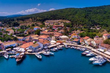 Fiskardo 'nun havadan görünüşü, Kefalonia. Turkuaz sularla çevrili bir yarımadada yuva yapmış güzel bir köy. Renkli evler, küçük plajlar ve körfezdeki tekneler. Arkaplanda yemyeşil tepeler ve dağlar var.