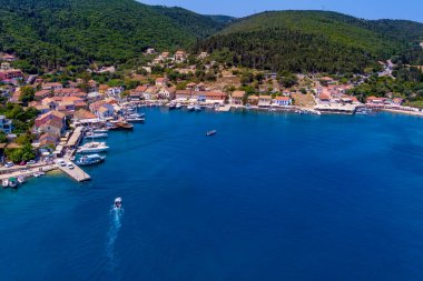 Fiskardo 'nun havadan görünüşü, Kefalonia. Turkuaz sularla çevrili bir yarımadada yuva yapmış güzel bir köy. Renkli evler, küçük plajlar ve körfezdeki tekneler. Arkaplanda yemyeşil tepeler ve dağlar var.