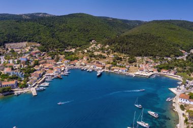 Fiskardo 'nun havadan görünüşü, Kefalonia. Turkuaz sularla çevrili bir yarımadada yuva yapmış güzel bir köy. Renkli evler, küçük plajlar ve körfezdeki tekneler. Arkaplanda yemyeşil tepeler ve dağlar var.