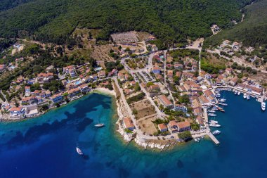 Fiskardo 'nun havadan görünüşü, Kefalonia. Turkuaz sularla çevrili bir yarımadada yuva yapmış güzel bir köy. Renkli evler, küçük plajlar ve körfezdeki tekneler. Arkaplanda yemyeşil tepeler ve dağlar var.