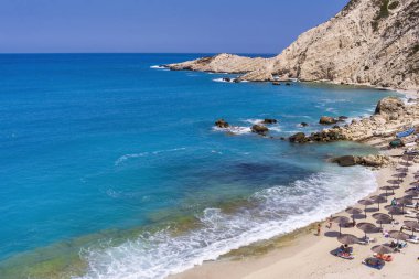 Petani Beach in Kefalonia features turquoise waters, golden sand, and is surrounded by cliffs. It's ideal for swimming and relaxing, with sunbeds and nearby tavernas clipart