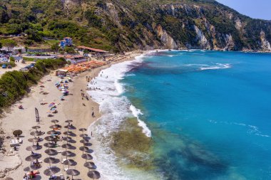 Petani Beach in Kefalonia features turquoise waters, golden sand, and is surrounded by cliffs. It's ideal for swimming and relaxing, with sunbeds and nearby tavernas clipart