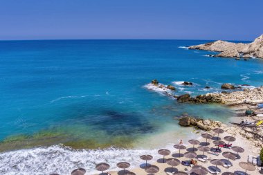 Petani Beach in Kefalonia features turquoise waters, golden sand, and is surrounded by cliffs. It's ideal for swimming and relaxing, with sunbeds and nearby tavernas clipart