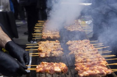 A grill filled with skewers of meat cooking over open flames. Smoke rises as the meat browns, while someone tends to the grill wearing gloves. The scene shows a traditional barbecue in progress.Greek Souvlaki clipart