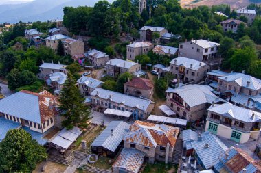 An aerial view of Nymfaio, a picturesque mountain village in Greece, surrounded by lush green forests and hills. The village's traditional stone houses with metal roofs are nestled into the scenic landscape. clipart