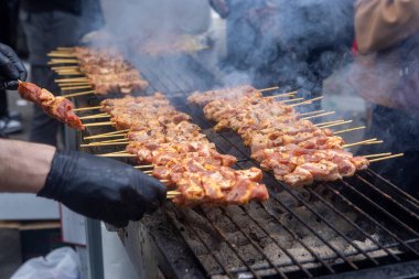 A grill filled with skewers of meat cooking over open flames. Smoke rises as the meat browns, while someone tends to the grill wearing gloves. The scene shows a traditional barbecue in progress. clipart