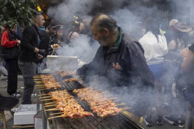 Selanik, Yunanistan - 7 Mart 2024: Tsiknopempti sırasında, et ızgarasıyla bilinen bir Yunan kutlaması sırasında, yaşlı bir adam dumanlı bir açık hava barbeküsünde sayısız şiş yapma eğilimindedir. Millet, şenlikli atmosferin tadını çıkarın.