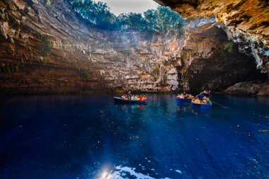 Kefalonia, Yunanistan - 25 Temmuz 2024: Kefalonya 'nın ünlü bir mücevheri olan Melissani Mağarası ve Göl, ziyaretçileri kristal berrak sularını tekneyle keşfetmeleri için ağırlayarak, şaşırtıcı bir ışık etkileşimi ortaya çıkardı.
