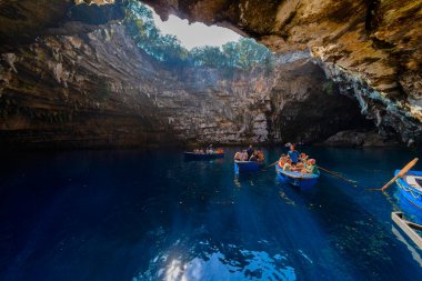 Kefalonia, Yunanistan - 25 Temmuz 2024: Kefalonya 'nın ünlü bir mücevheri olan Melissani Mağarası ve Göl, ziyaretçileri kristal berrak sularını tekneyle keşfetmeleri için ağırlayarak, şaşırtıcı bir ışık etkileşimi ortaya çıkardı.