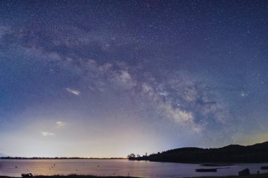 Samanyolu Kerkini Gölü 'nün durgun suları üzerinde parlak bir şekilde parıldıyor. Yalnız bir tekne, doğanın barışçıl kucaklamalarıyla nazikçe sürüklenir. Yıldızların yansıması rüya gibi atmosferi güçlendirir.