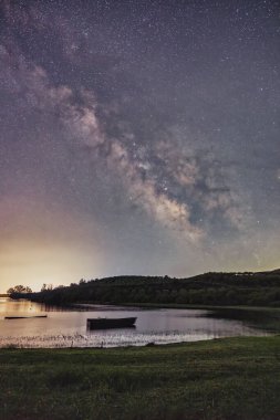Samanyolu Kerkini Gölü 'nün durgun suları üzerinde parlak bir şekilde parıldıyor. Yalnız bir tekne, doğanın barışçıl kucaklamalarıyla nazikçe sürüklenir. Yıldızların yansıması rüya gibi atmosferi güçlendirir.